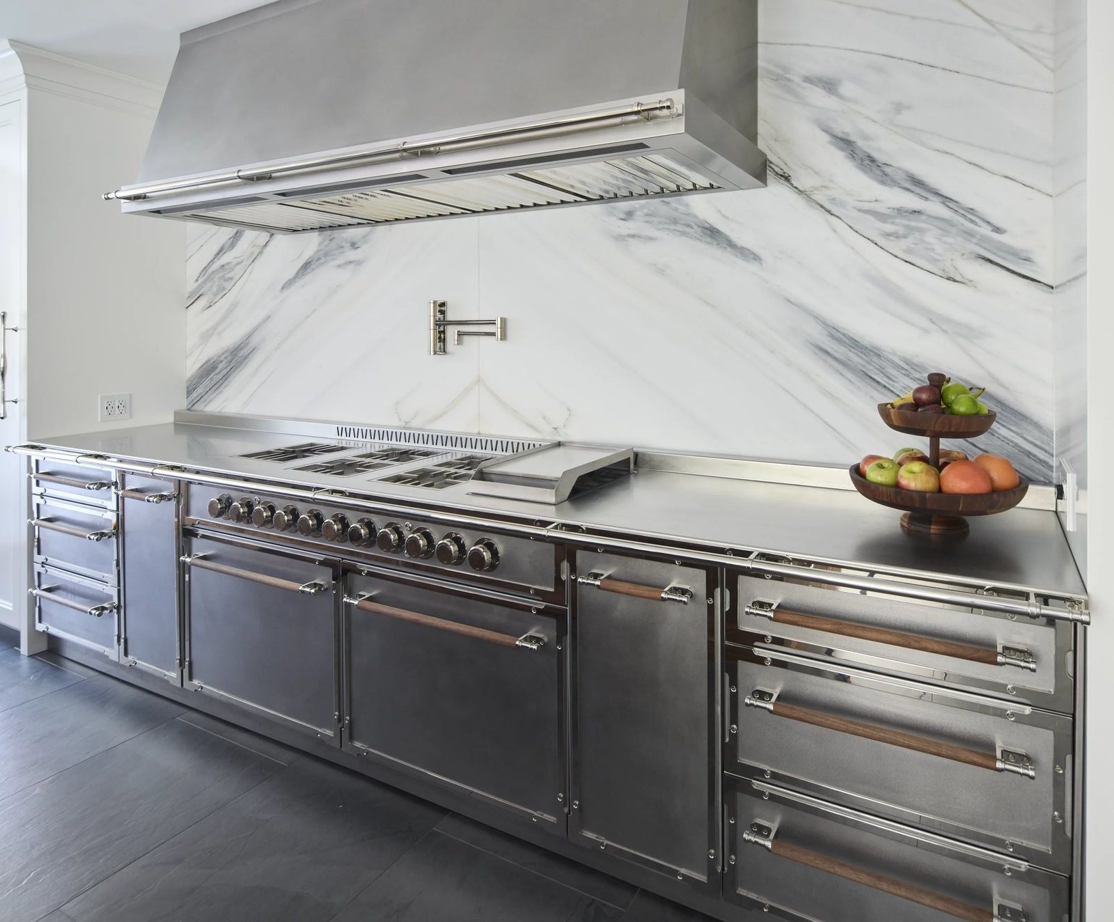 Custom stainless French range with matching hood built precisely into a marble backsplash and countertop