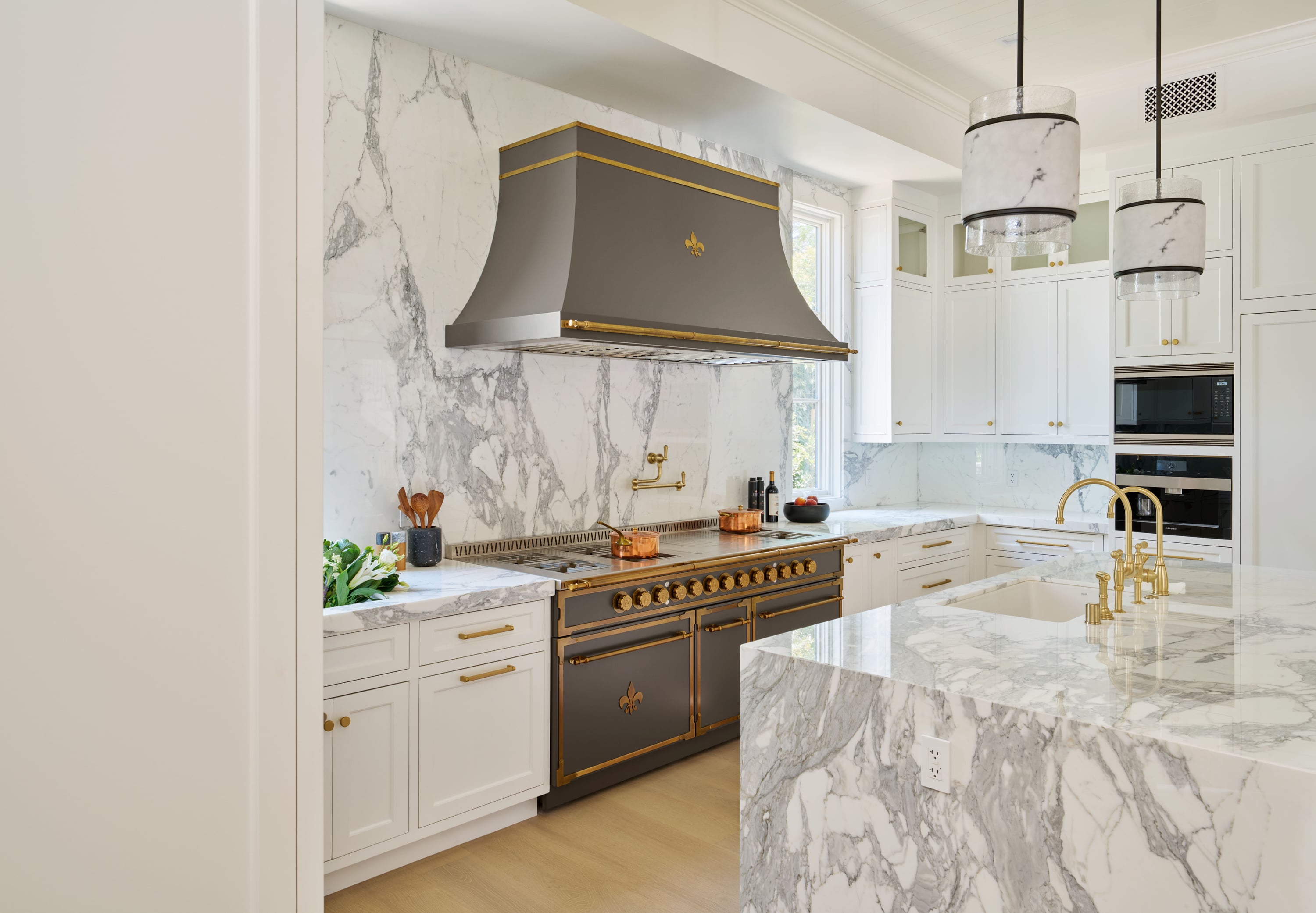 Luxury kitchen featuring a midnight matte professional range with brushed brass trim, a matching hood, and a dramatic white marble backsplash.